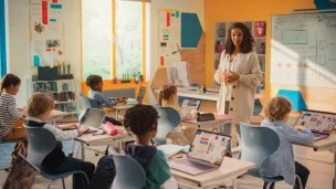 Teacher leading class in tech-filled, bright classroom.