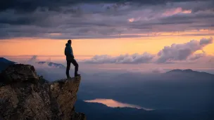 Man on cliff overlooking lake at sunset.