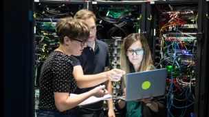 Three people working on servers, photograph.