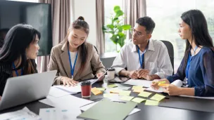 Four professionals collaborate around a table with papers and sticky notes.