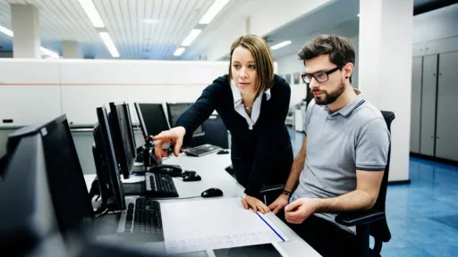 A woman instructs a man, pointing to a computer screen.