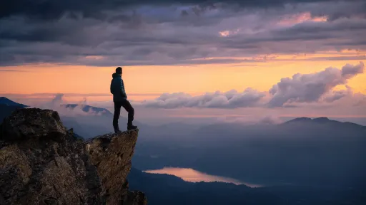 Man on cliff overlooking lake at sunset.