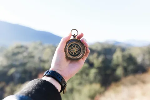 Hand holds compass, mountain background.