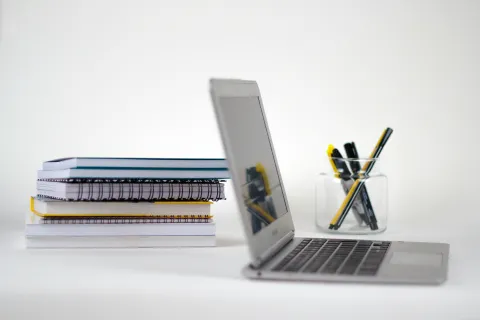 Laptop next to notebooks and pen holder.