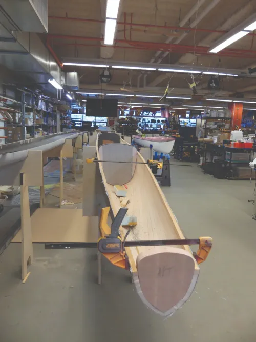 A simple wooden boat is in a large workshop.