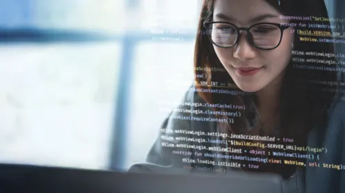 Young woman with glasses codes at a laptop.