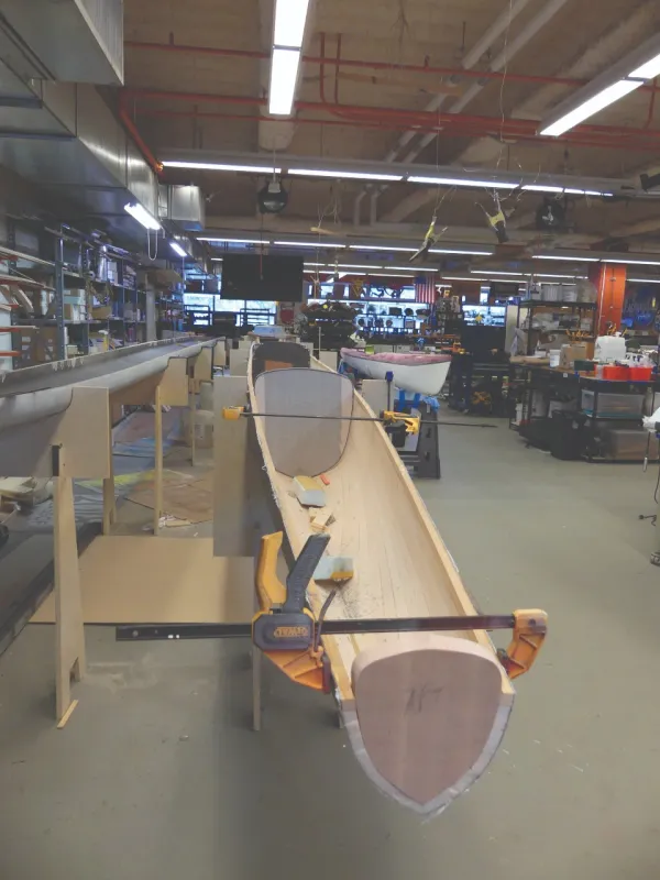 A simple wooden boat is in a large workshop.